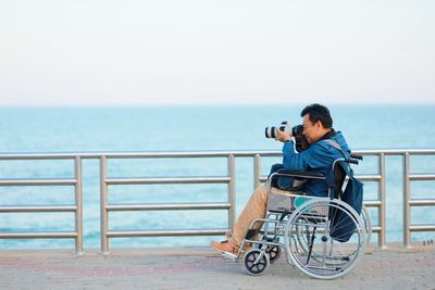 Man photographing on railing by sea against sky
