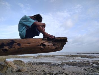 Man sitting on rock at beach against sky