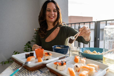 Attractive middle-aged woman eating chinese take away food sitting at a laid table in a city balcony