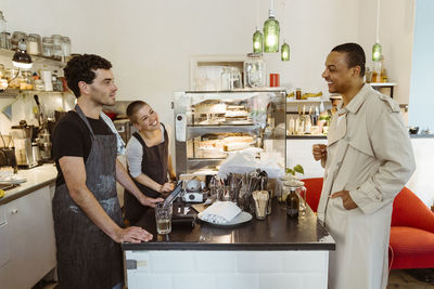 Smiling customer interacting with male and female cafe owners at checkout counter