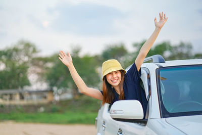 Young woman smiling while sitting on car against sky