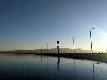 Silhouette street by lake against sky during sunset
