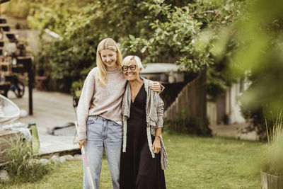 Smiling granddaughter with arm around grandmother standing in back yard