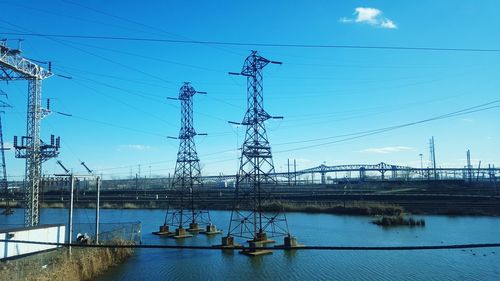 Electricity pylons in river against sky