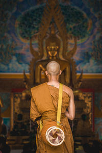 Rear view of monk standing against buddha statue in temple