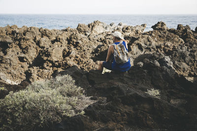 Rear view of woman sitting on rock at beach