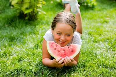 Cute girl lying on grass eating watermelon