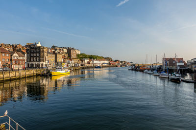 Sailboats moored on canal by buildings in city against sky