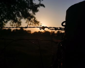 Close-up of silhouette barbed wire against sky during sunset