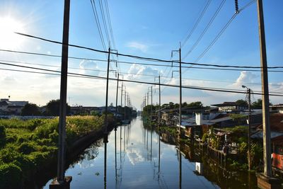 Reflection of electricity pylon in canal against sky