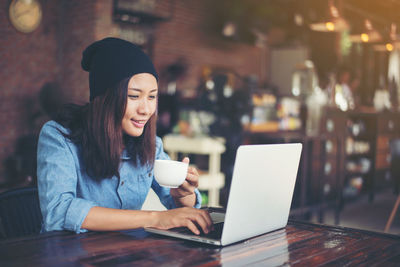 Smiling young woman using laptop on table at cafe