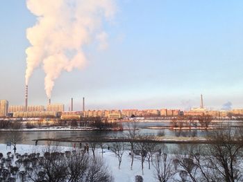 Smoke emitting from factory by river against sky