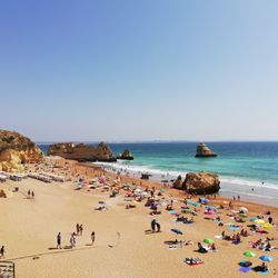 People at beach against clear sky during sunny day