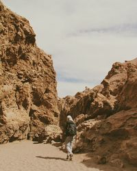 Rear view of man walking on rock against sky