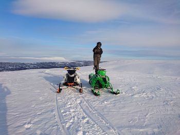 Full length of man standing by snowmobiles on snow against sky
