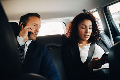 Businessman talking on mobile phone while sitting by female colleague in taxi
