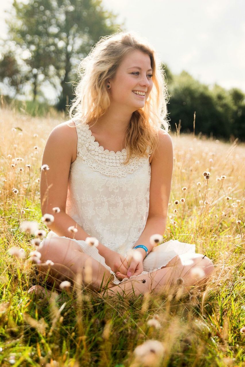 person, young adult, young women, grass, portrait, leisure activity, looking at camera, lifestyles, casual clothing, focus on foreground, three quarter length, long hair, field, front view, smiling, sitting, relaxation