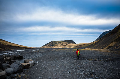 Rear view of hiker walking on landscape against sky