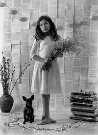 Portrait of girl holding flowers while standing by chihuahua against wall