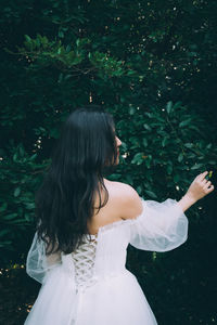 Rear view of woman with arms raised standing against plants