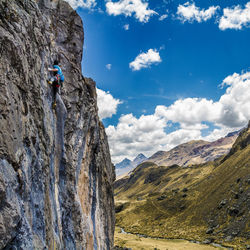Low angle view of man climbing on cliff against sky