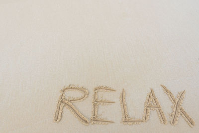 High angle view of relax written on sand at beach