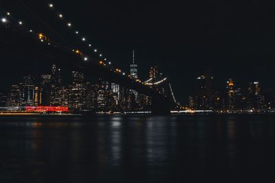 Illuminated city by river against sky at night