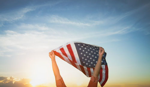 Low angle view of person holding flag against sky during sunset