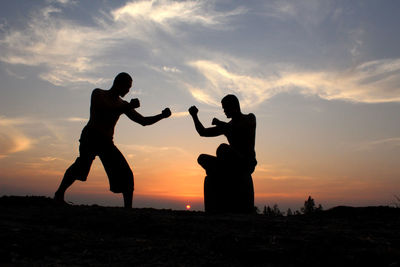 Silhouette men practicing boxing against orange sky during sunset