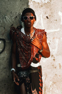 Young man wearing sunglasses standing against wall