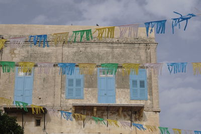 Low angle view of bunting flags by building against cloudy sky