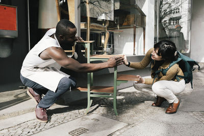 Upcycling store owner showing furniture to female customer at sidewalk