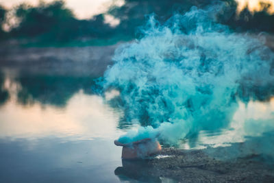 Flower pot emitting smoke by lake during sunset