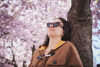 Young woman standing under cherry blossom