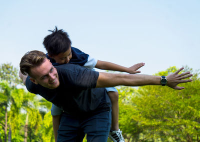 Father playing with son at park against clear sky