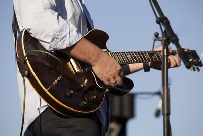 Midsection of man playing guitar while standing against sky