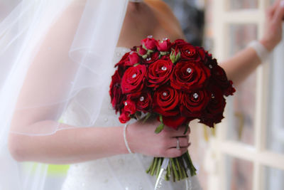 Midsection of bride holding red roses