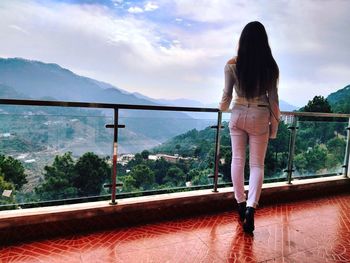 Rear view of woman standing by railing against mountain