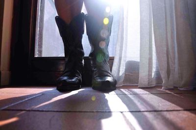 Low section of person standing in cowboy boots by window at home