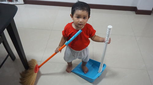 Full length portrait of cute boy with broom and dustpan at home