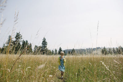 Girl walking on grassy field against clear sky