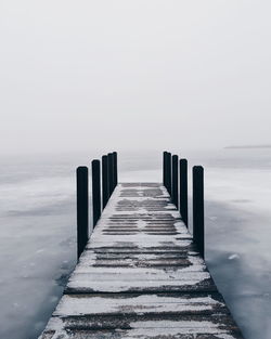 Wooden posts in sea against sky during winter