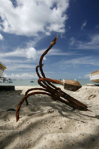 Rusty anchor at beach against sky
