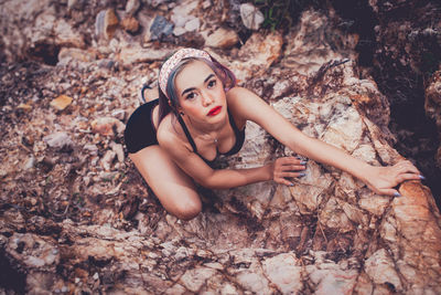 Portrait of young woman lying on rock against tree trunk