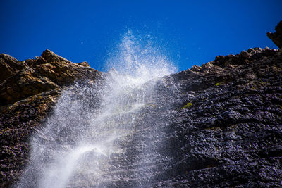 Low angle view of waterfall against blue sky