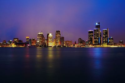 Scenic view of river by illuminated urban skyline against sky