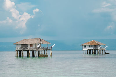 Stilt house on sea by building against sky