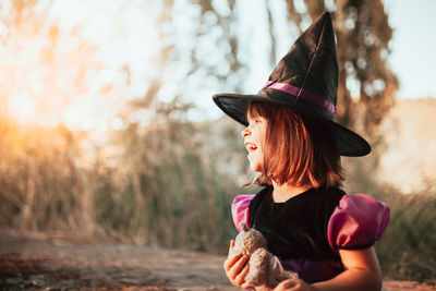 Smiling girl wearing witchs hat during halloween at forest