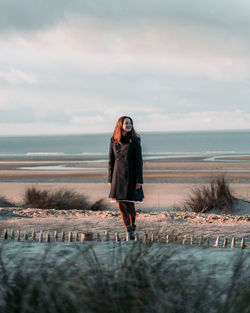 Woman standing on sea shore against sky