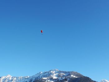 Low angle view of people paragliding against clear blue sky